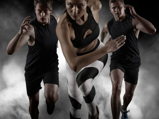 Sporty young woman and men running on black background