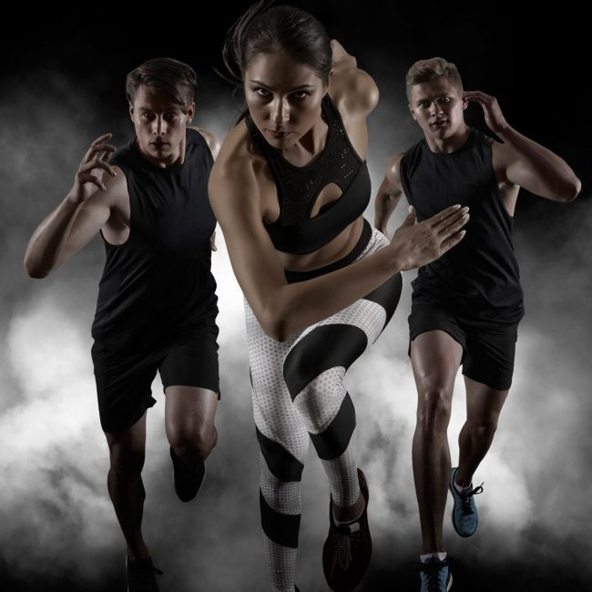 Sporty young woman and men running on black background